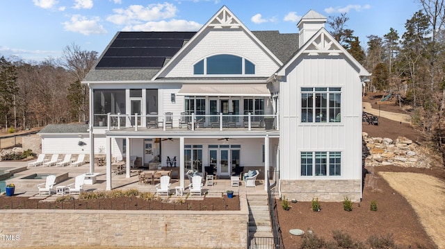 back of house with a ceiling fan, a sunroom, a patio area, board and batten siding, and roof mounted solar panels