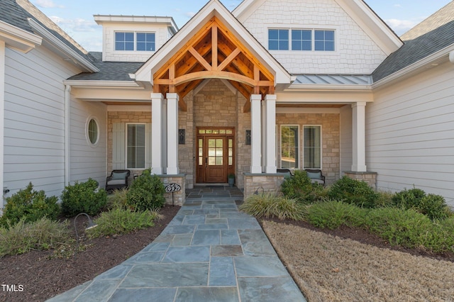 view of exterior entry featuring a porch, stone siding, and a shingled roof