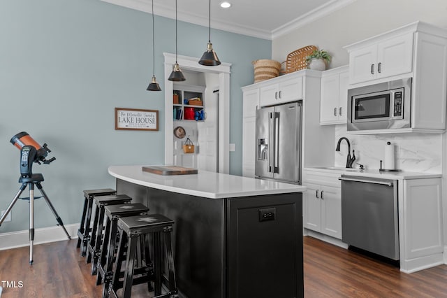 kitchen with a kitchen island, a sink, ornamental molding, light countertops, and stainless steel appliances