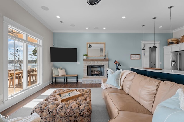 living room featuring recessed lighting, a stone fireplace, wood finished floors, and crown molding