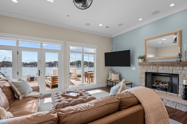 living room featuring wood finished floors, baseboards, a fireplace, ornamental molding, and a water view