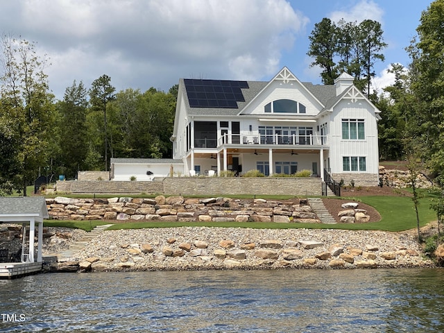 back of house featuring roof mounted solar panels, stairway, a water view, and a sunroom