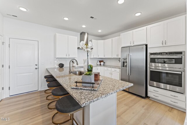 kitchen with wall chimney range hood, visible vents, a sink, stainless steel appliances, and a kitchen breakfast bar