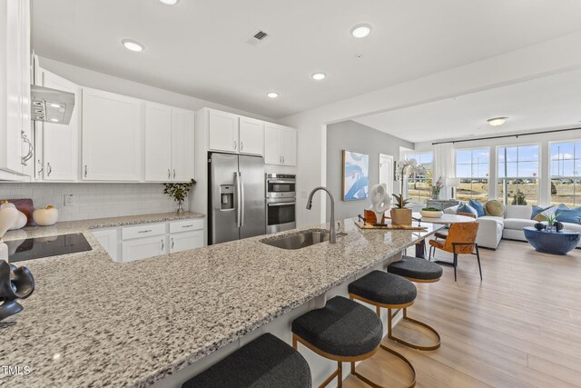 kitchen with light stone counters, visible vents, a sink, decorative backsplash, and stainless steel appliances