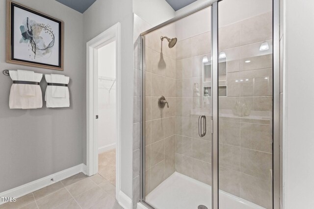 bathroom featuring tile patterned floors, a stall shower, a spacious closet, and baseboards