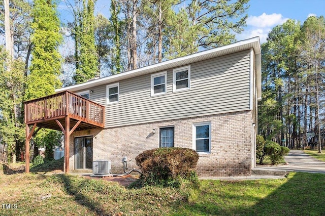 back of property with brick siding, central air condition unit, a wooden deck, and a yard