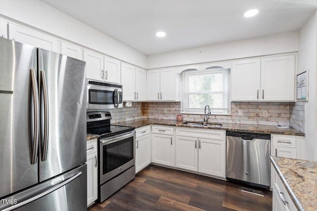 kitchen featuring a sink, backsplash, stone counters, appliances with stainless steel finishes, and dark wood-style flooring