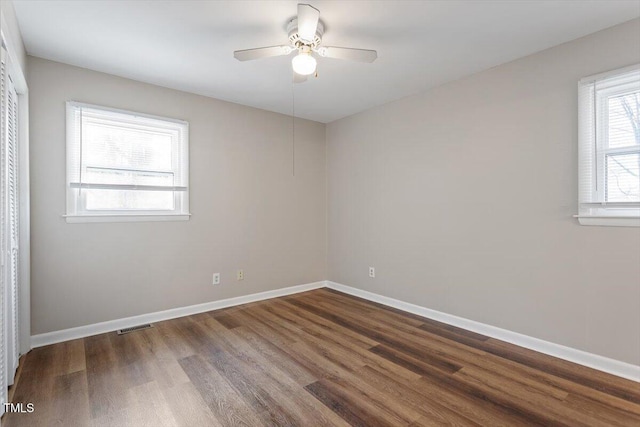 empty room with dark wood-style floors, visible vents, ceiling fan, and baseboards