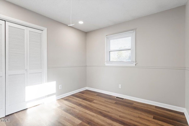 unfurnished bedroom featuring visible vents, wood finished floors, baseboards, and a closet