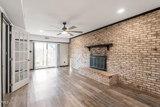 unfurnished living room featuring ceiling fan, wood finished floors, a brick fireplace, and brick wall