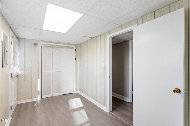 unfurnished bedroom with baseboards, wood finished floors, a closet, and a paneled ceiling