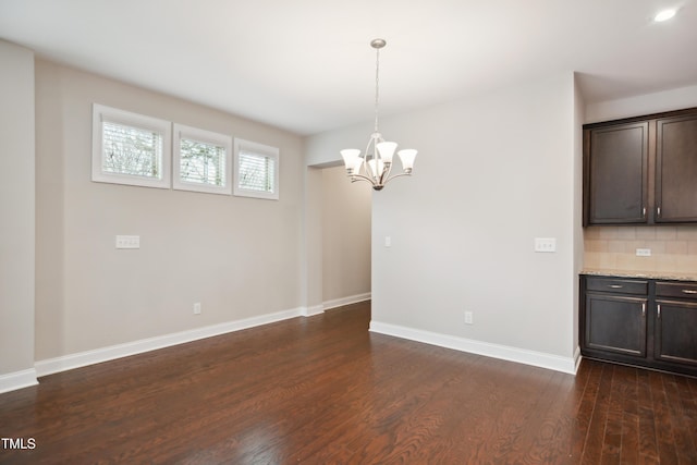 unfurnished dining area featuring a chandelier, baseboards, and dark wood-style floors