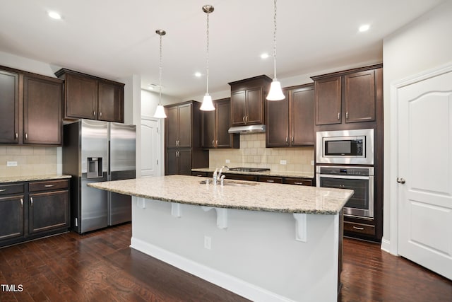 kitchen featuring dark brown cabinetry, under cabinet range hood, a breakfast bar area, appliances with stainless steel finishes, and a sink