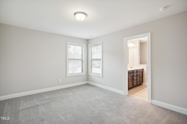 unfurnished bedroom featuring baseboards, light colored carpet, and ensuite bathroom