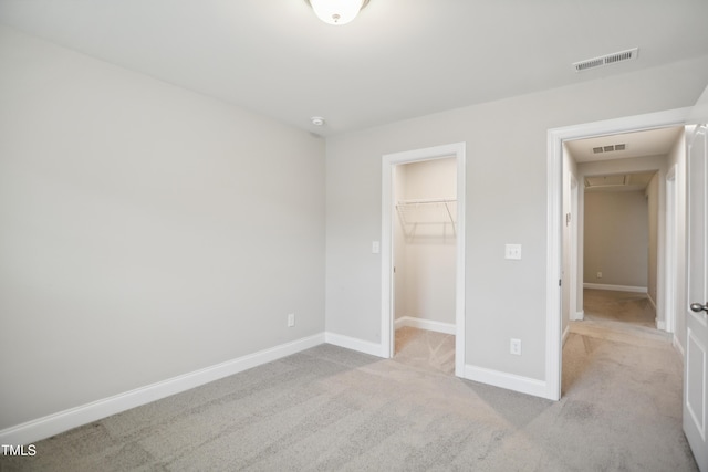 unfurnished bedroom featuring a walk in closet, carpet, visible vents, and baseboards