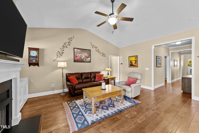 living area with a fireplace with flush hearth, lofted ceiling, wood finished floors, baseboards, and ceiling fan