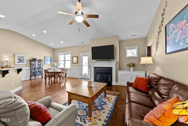 living room featuring wood finished floors, wainscoting, a fireplace, lofted ceiling, and ceiling fan