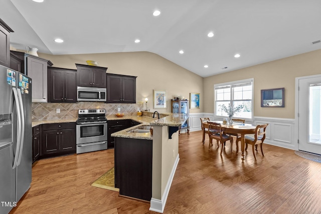 kitchen featuring vaulted ceiling, light stone counters, appliances with stainless steel finishes, a peninsula, and a sink