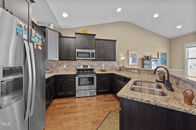 kitchen with light stone countertops, vaulted ceiling, light wood-style flooring, appliances with stainless steel finishes, and a sink