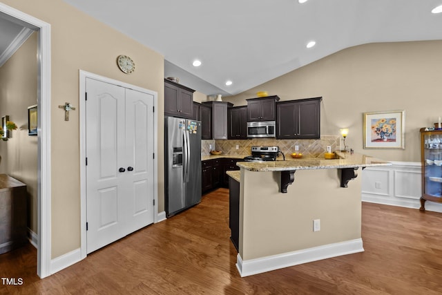 kitchen featuring lofted ceiling, wood finished floors, appliances with stainless steel finishes, a breakfast bar area, and light stone countertops