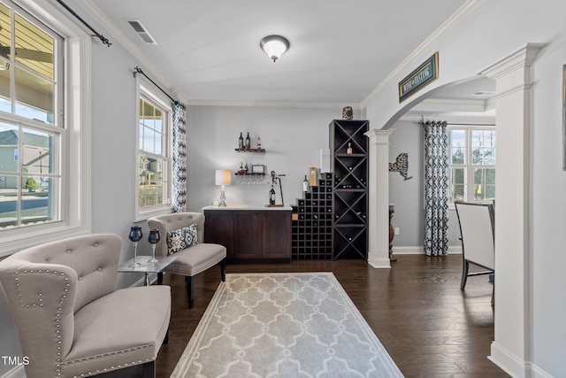 living area featuring visible vents, decorative columns, arched walkways, dark wood-style flooring, and crown molding