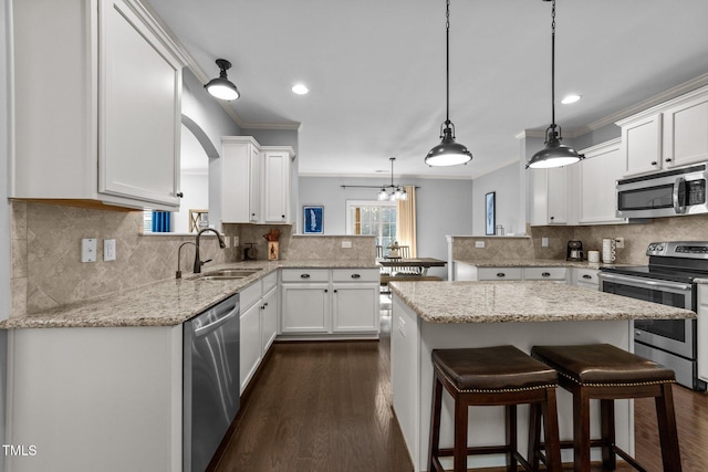 kitchen with crown molding, appliances with stainless steel finishes, a peninsula, white cabinetry, and a sink