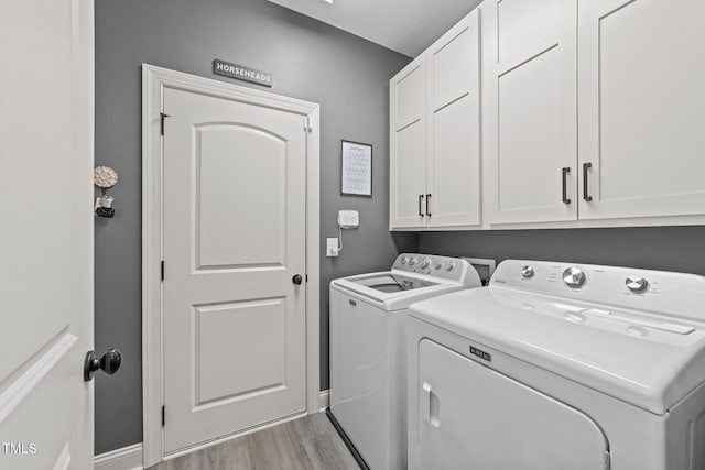 clothes washing area with light wood finished floors, washing machine and dryer, cabinet space, and baseboards