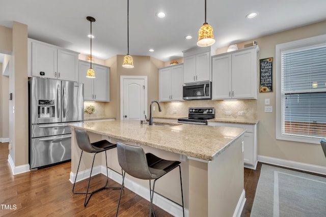 kitchen with a kitchen island with sink, a sink, dark wood-style floors, appliances with stainless steel finishes, and light stone countertops