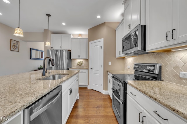 kitchen featuring pendant lighting, wood finished floors, white cabinets, stainless steel appliances, and a sink