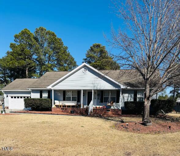 ranch-style home featuring a garage, a porch, and a front lawn