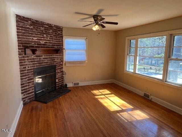 unfurnished living room with visible vents, a brick fireplace, baseboards, and wood finished floors