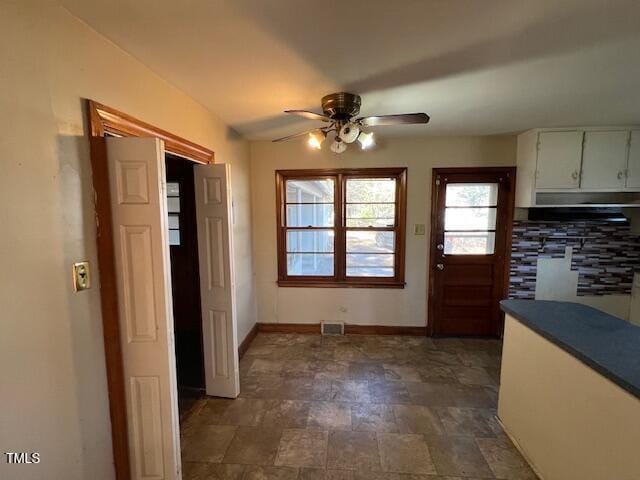 doorway featuring stone finish flooring, baseboards, visible vents, and a ceiling fan