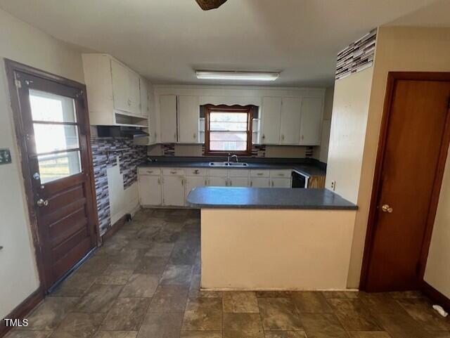 kitchen featuring baseboards, a peninsula, a sink, white cabinets, and dark countertops