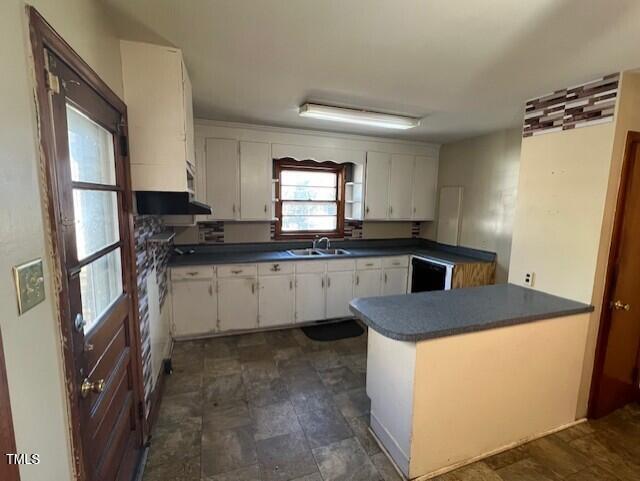 kitchen with dark countertops, dishwasher, a peninsula, white cabinets, and a sink