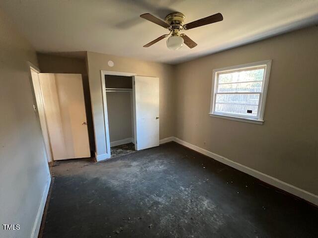 unfurnished bedroom featuring unfinished concrete flooring, a ceiling fan, baseboards, and a closet