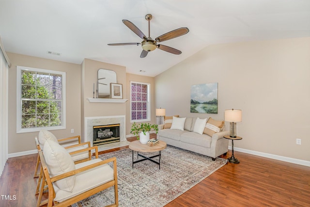 living area with visible vents, baseboards, lofted ceiling, a premium fireplace, and wood finished floors