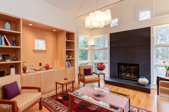 living area with a glass covered fireplace, an inviting chandelier, built in shelves, and wood finished floors