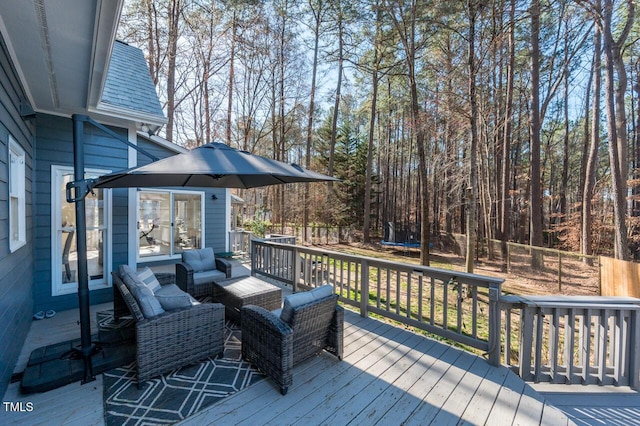 wooden deck featuring a trampoline, outdoor lounge area, and fence