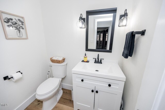 half bath featuring vanity, toilet, wood finished floors, and baseboards