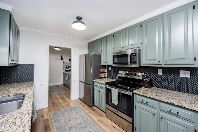 kitchen featuring baseboards, light wood finished floors, appliances with stainless steel finishes, crown molding, and backsplash