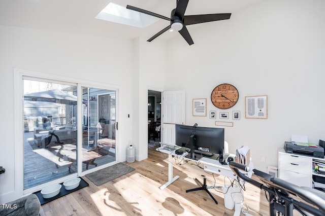 home office featuring a ceiling fan, a skylight, wood finished floors, and a towering ceiling