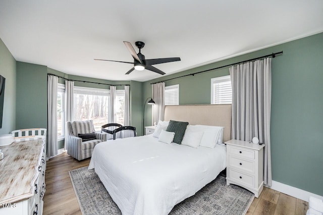 bedroom featuring multiple windows, baseboards, ceiling fan, and wood finished floors