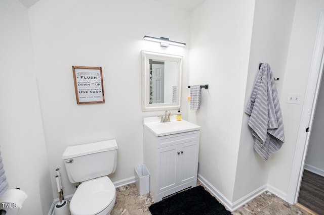 half bathroom with vanity, toilet, and baseboards