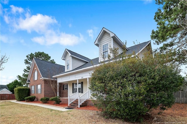 cape cod house featuring brick siding, a porch, fence, and a front lawn