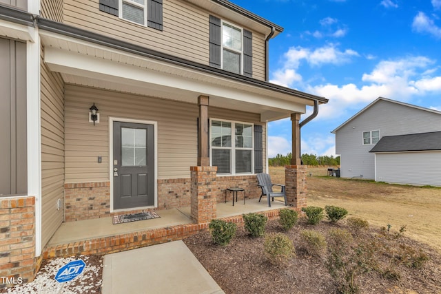 view of exterior entry with brick siding and covered porch