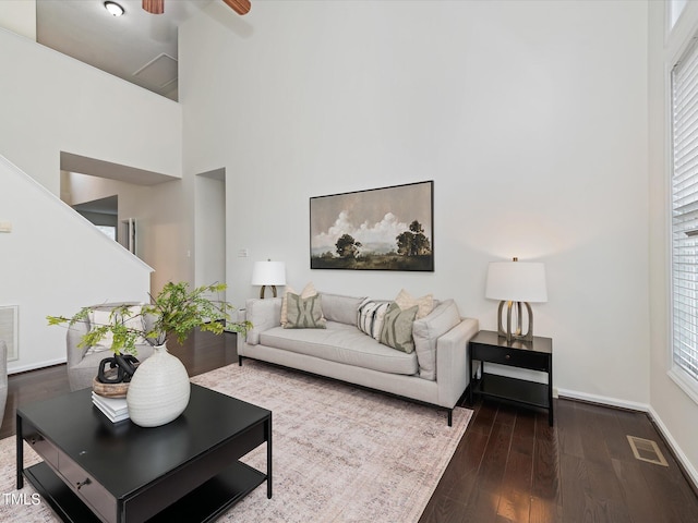 living area featuring visible vents, ceiling fan, baseboards, a high ceiling, and wood finished floors