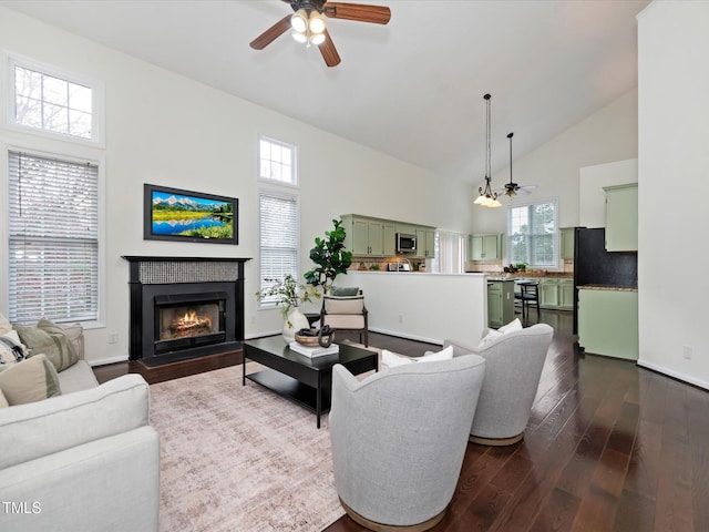 living area with baseboards, ceiling fan, a fireplace with flush hearth, high vaulted ceiling, and dark wood-style flooring