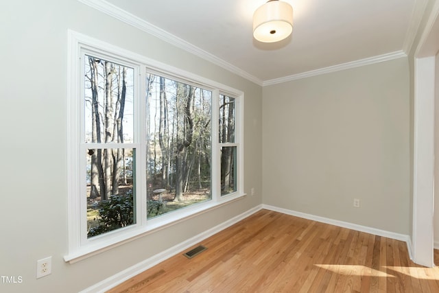 spare room with crown molding, light wood-style flooring, baseboards, and visible vents