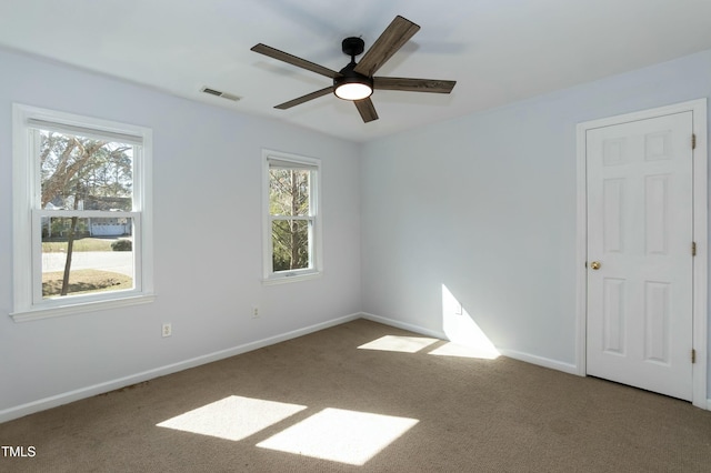 carpeted spare room with visible vents, a healthy amount of sunlight, a ceiling fan, and baseboards