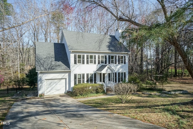 colonial home with driveway, fence, an attached garage, a shingled roof, and a chimney